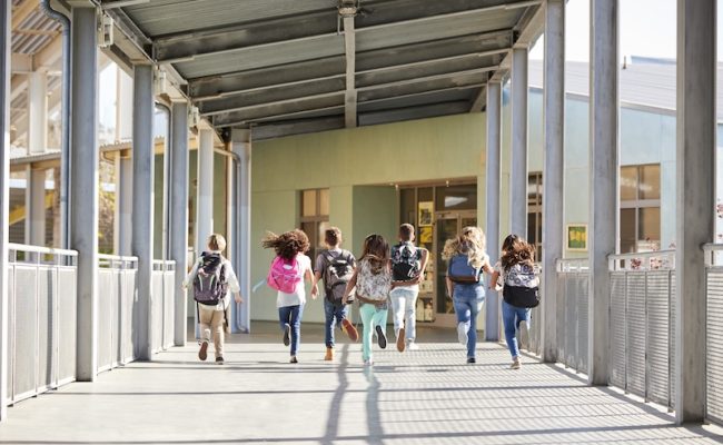 Elementary school kids running in school corridor, back view